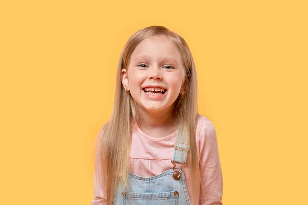 Portret van een blond meisje dat glimlacht en naar de camera kijkt. Gele achtergrond. — Stockfoto