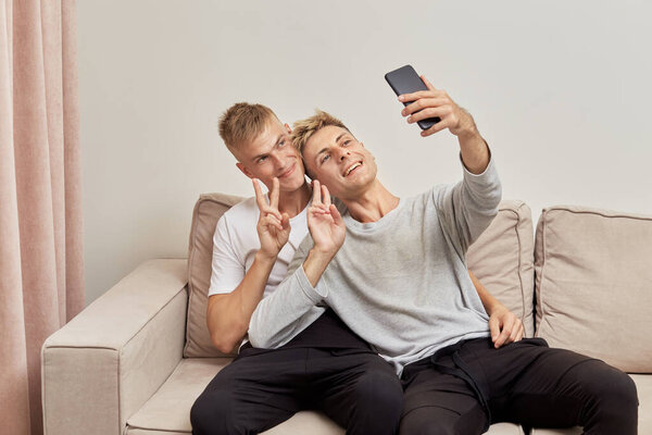 LGBT couple show a gesture to the world and look at the smartphone camera.