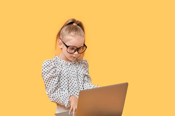 Cute baby girl in a shirt looks at an open laptop. Large glasses for vision. — Stock Photo, Image