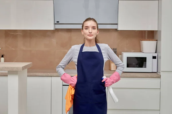 Egy fiatal nő a kamerába néz, miközben takarít a konyhában.. — Stock Fotó