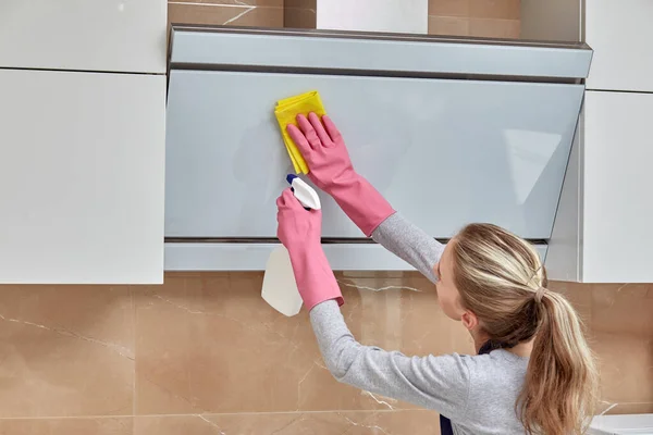 A young woman cleans to get household chemicals in the kitchen in a can.