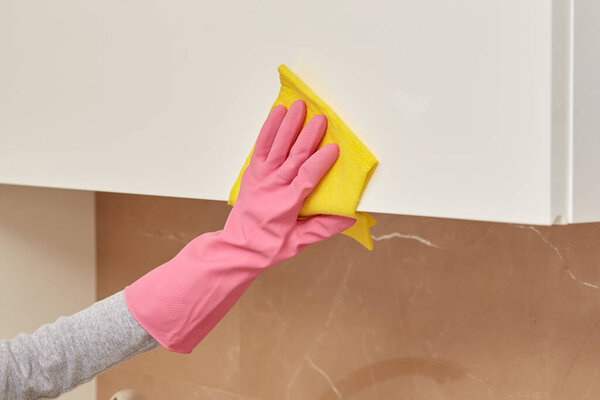 Womens hands in pink rubber gloves do the cleaning with a yellow napkin.