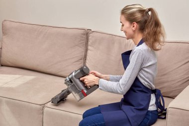 Genç bir kadın kanepeyi elektrikli süpürgeyle yıkıyor, arkadan görüyor..