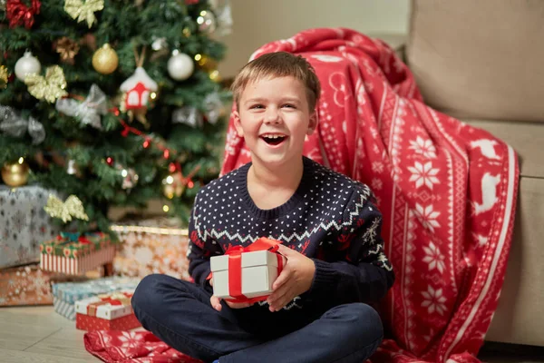 Um menino rindo em uma camisola tem um presente em sua mão. — Fotografia de Stock