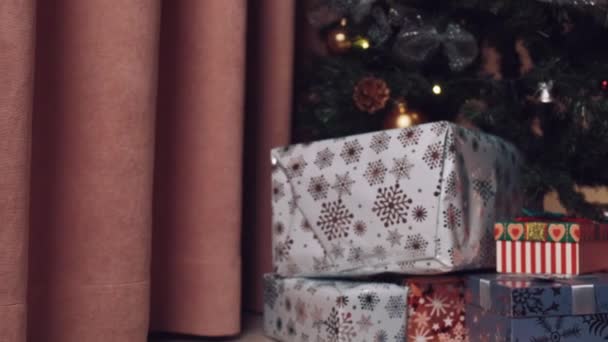 O menino fica perto da árvore de Natal e olha para os presentes nas caixas. — Vídeo de Stock