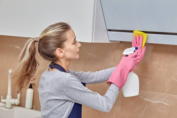 Woman cleaner washes the hood in the kitchen with household chemicals in spray.