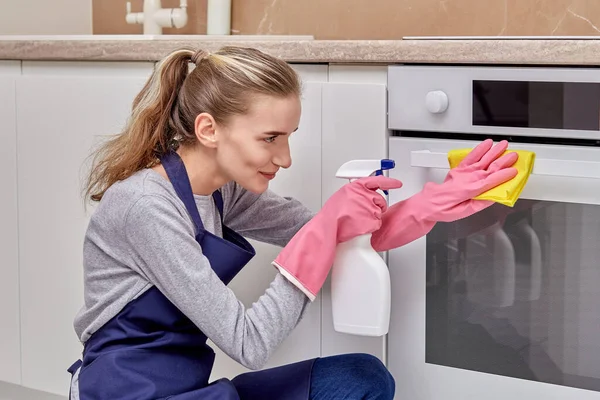 若い女性は台所をきれいにし、電気ストーブを洗剤で洗います. — ストック写真