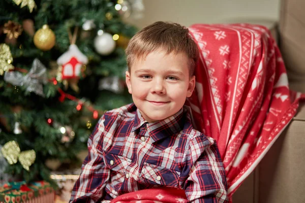Um lindo menino olha para a câmera ao lado de uma árvore de Natal. — Fotografia de Stock