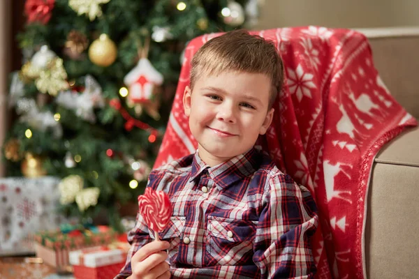 Um menino bonito segura um doce em um pau na mão e olha para a câmera. — Fotografia de Stock