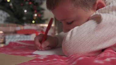 Tatlı çocuk Noel Baba 'ya Noel mektubu yazıyor. Battaniyenin üzerinde yerde yatıyor..