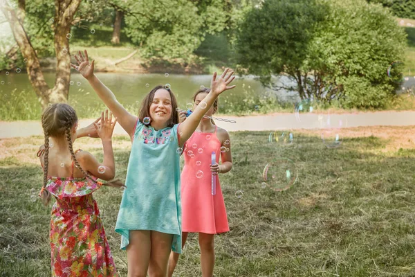 Meninas bonitas brincam juntas no parque e sopram bolhas de sabão. — Fotografia de Stock