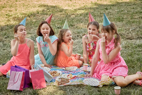 Små flickor i partyhattar firar sin födelsedag på sommaren på en picknick. — Stockfoto