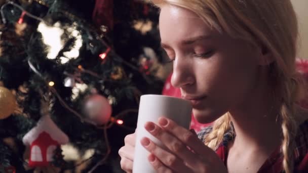 Young blonde woman in pajamas drinking hot chocolate on Christmas night. — Stock Video