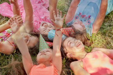 Tatil şapkalı, kirli yüzlü komik kızlar çimlerin üzerinde birlikte yatıyorlar..