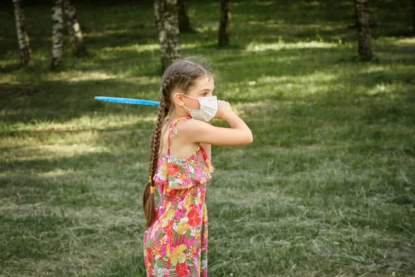 Uma menina com cabelos longos em uma máscara médica com uma raquete de badminton em suas mãos. — Fotografia de Stock