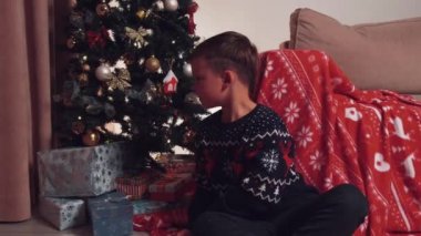 Çocuk etrafına bakıyor ve bir Noel hediyesi açıyor, içinde parlak mavi bir ışık parlıyor..