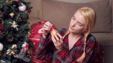 Genç ve güzel bir kadın ağaçlara altın bir Noel oyuncağı asıyor..