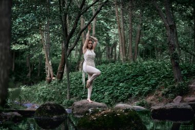 Elbiseli genç bir kadın bir kayanın üzerinde duruyor ve bir bacağında denge var..