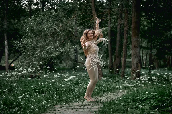 En flicka i beige kostym dekorerad med makramedans i skogen. Högt träd. — Stockfoto