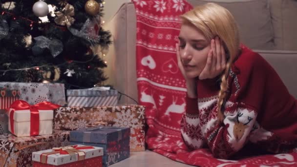 Ξανθιά γυναίκα ανοίγει ένα χριστουγεννιάτικο δώρο ξαπλωμένη στο πάτωμα κοντά στο χριστουγεννιάτικο δέντρο. — Αρχείο Βίντεο
