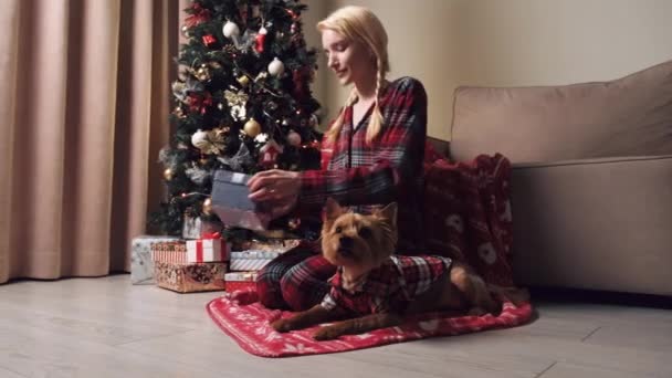 Junge blonde Frau öffnet eine Geschenkbox. In der Nähe liegt ein kleiner süßer Hund Pommern. — Stockvideo
