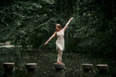 Elbise giymiş genç bir kadın beton bir çemberin üzerinde duruyor ve dengesini koruyor..