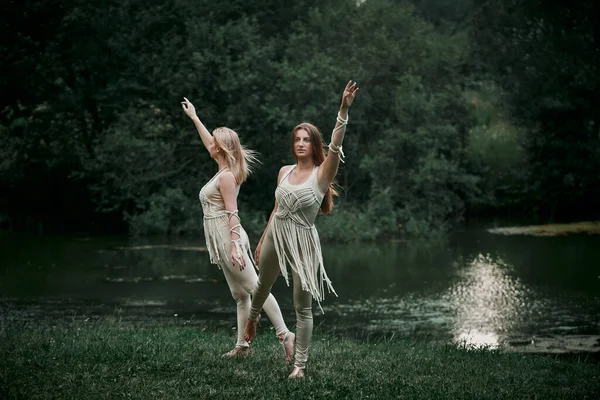 Två vackra unga kvinnor som dansar i naturen. Det finns en stor sjö bakom. — Stockfoto