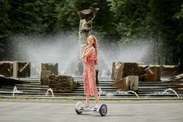Een tiener meisje in een jumpsuit op een gyro scooter, hoverboard in een zomer park. — Stockfoto