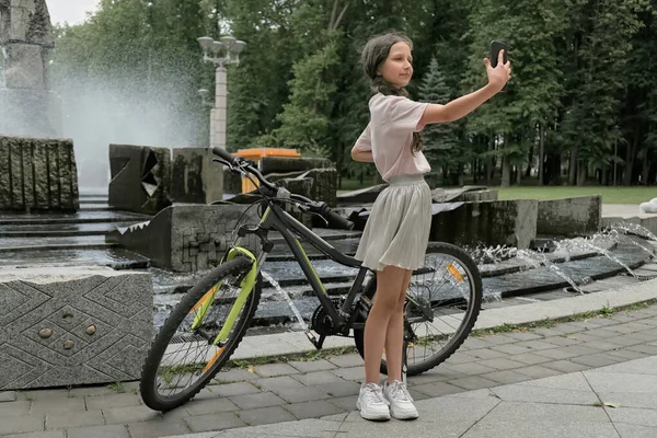 Милая девушка в короткой юбке делает селфи возле фонтана в парке. — стоковое фото