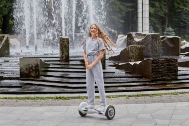 Bir kız jiroskop sürüyor, yazın uçan kaykay sürüyor ve kameraya bakıyor..