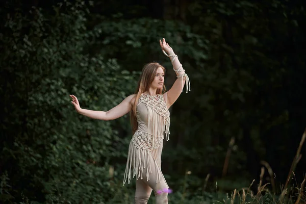 Une jeune femme danse dans un costume décoré de macramé, derrière une forêt sombre. — Photo