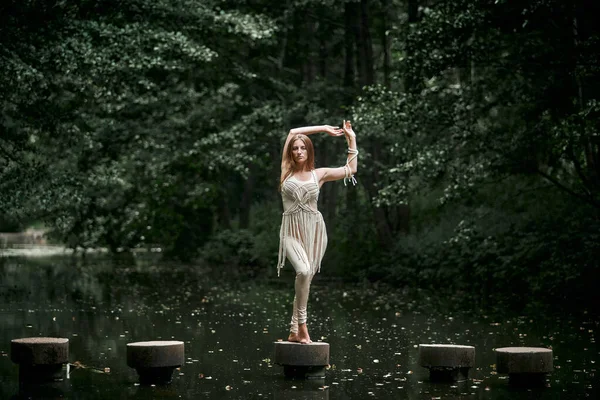 En kvinna i klänning står på en betongcirkel i vattnet, håller balansen. — Stockfoto