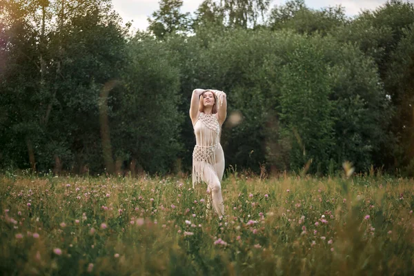Femme dans une robe beige dansant dans un champ avec des fleurs, macramé dans des vêtements. — Photo