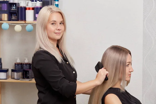 Een vrouwelijke kapper kamt haar blonde haar met een kam en kijkt naar de camera. — Stockfoto