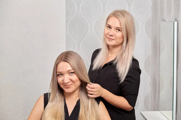 En kvindelig frisør ordner sit hår for en klient. Smukt sundt blondt hår. - Stock-foto