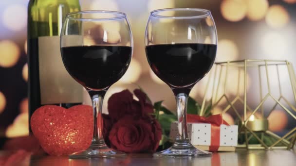 Dois copos de vinho tinto. As penas vermelhas caem de cima. Cenário romântico. — Vídeo de Stock