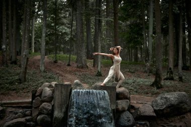 Uzun saçlı bir kadın çeşmenin üstünde dans ediyor. Elbise makromdan yapılmış.