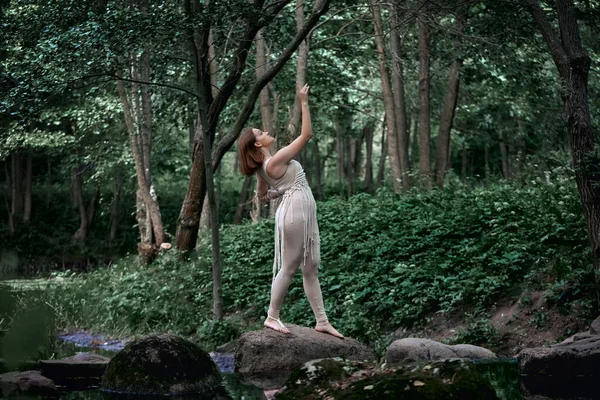 En ung vacker kvinna i klänning står barfota på en sten och dansar. — Stockfoto