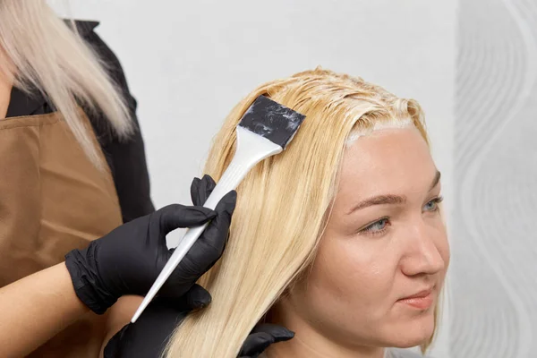 Handen van een vrouwelijke kapper in zwarte handschoenen, verven het haar van een klant. — Stockfoto