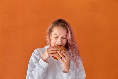 Diyet yapan bir kadın iştahlı büyük bir hamburger yer. Turuncu arkaplan.