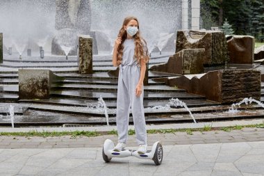 Bir kız yazın jiroskopa biniyor, sağlık maskesi takıyor..