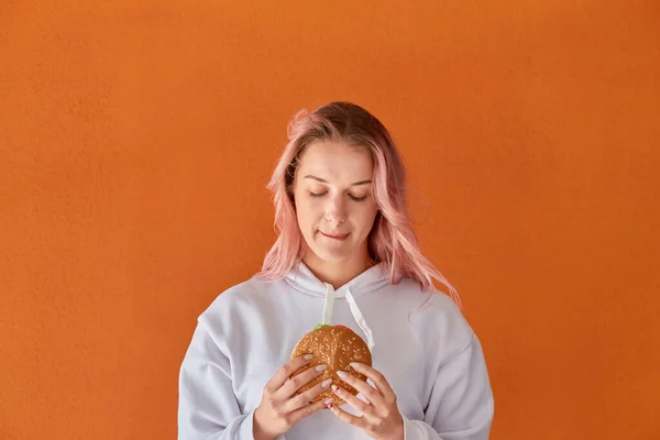 Mladá žena drží velký lahodný hamburger. oranžové pozadí. — Stock fotografie