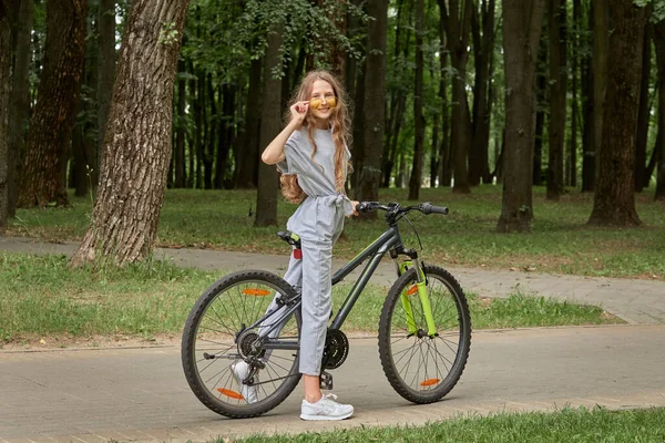 Дівчина в сонцезахисних окулярах їде на велосипеді в парку влітку. Зовнішня діяльність . — стокове фото