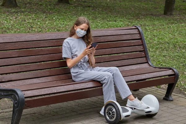 A menina senta-se em um banco e comunica-se em redes sociais com um telefone celular — Fotografia de Stock