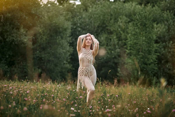 Ung kvinna i klänning dansar på ett fält med blommor på en ljus solig dag. — Stockfoto