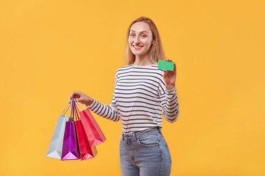 Elinde boş yeşil kartıyla alışveriş torbaları olan genç bir kadın..