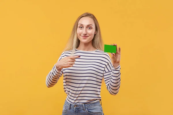 Una joven hermosa rubia señala una tarjeta verde vacía. — Foto de Stock