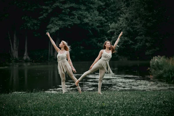 Les jeunes femmes en robes beiges se tiennent sur une jambe. Il y a un grand lac derrière. — Photo