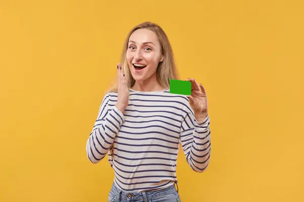 Una joven rubia sorprendida sostiene una tarjeta verde vacía en su mano. — Foto de Stock