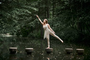 Elbiseli genç bir kadın suyun içinde bir çemberin üzerinde duruyor ve dengeyi sağlıyor..